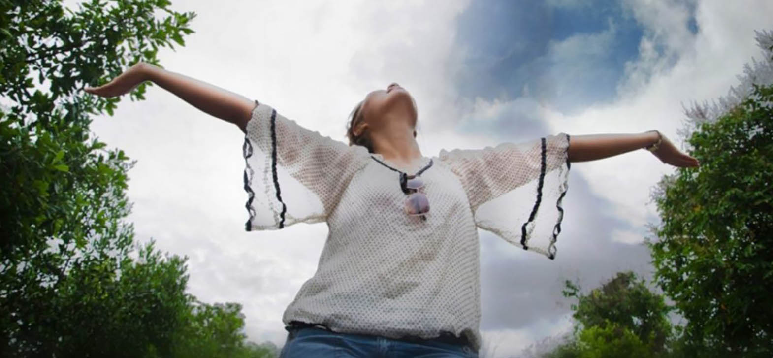 A student at Latham Centers enjoys the sun on a summer day, arms outstretched to the sky.