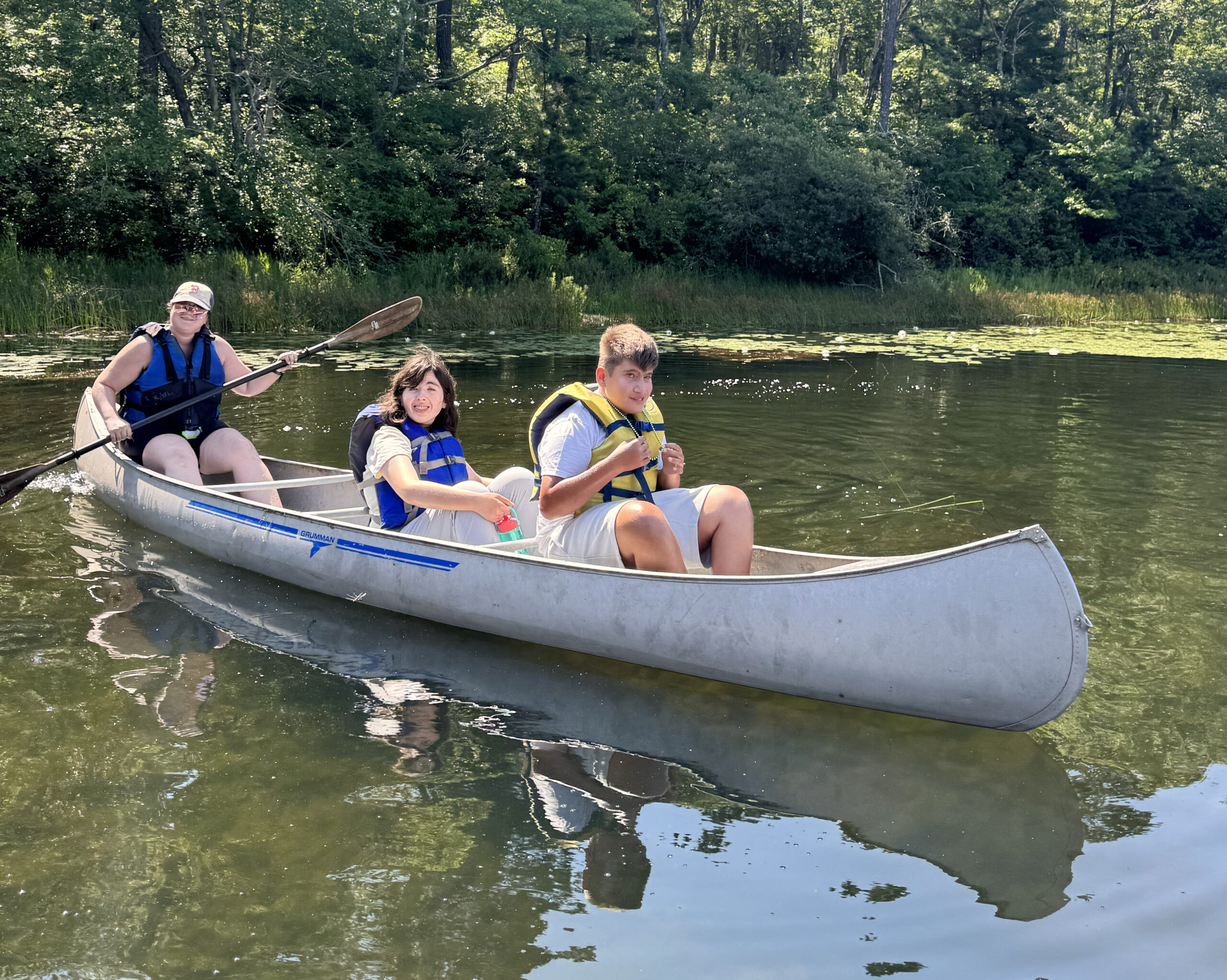 Three people wearing life vests in a canoe on a pond.